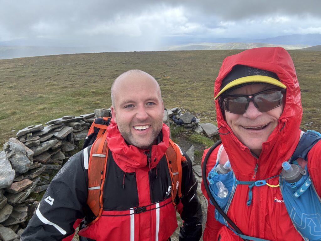 Mike and the other hiker in front of a short rock wall. Both are wearing rain soaked red jackets...and big smiles!