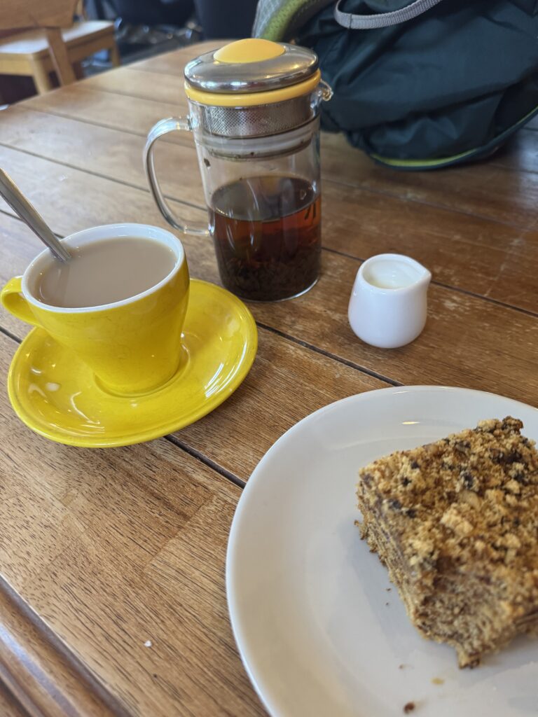 Table setting with small teapot, cup of tea with cream, and a honey cake on a plate...with a bite out of it ;) 