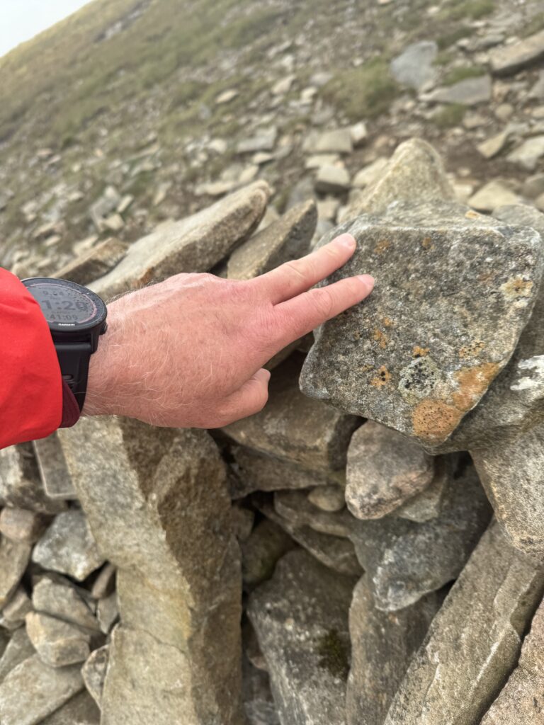Touching the established rock pile at the top of A' Mharconaich. Tapping with two fingers.